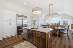 A modern kitchen with white cabinetry, a central island, and a dining area with wooden chairs and a table.