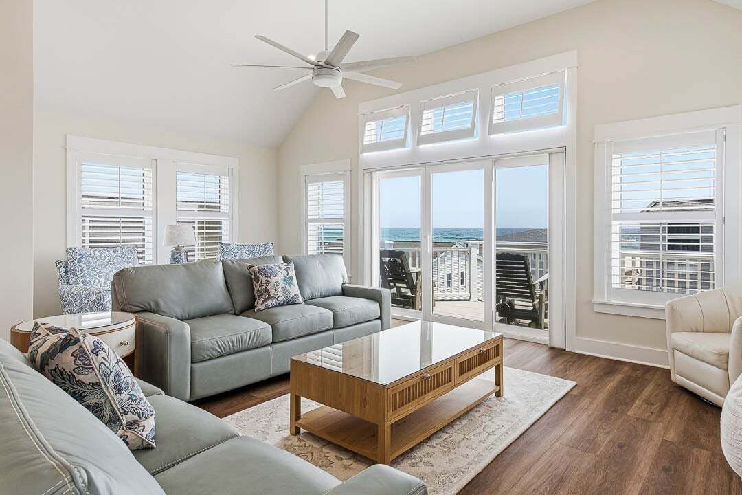 Ein geräumiges Wohnzimmer mit grauem Sofa, einem Holztisch und einem Deckenventilator.