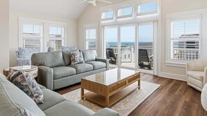 A spacious living room with a grey sofa, a wooden coffee table, and a ceiling fan. - Sandpiper Shore | 75 ft to the Beach | Brand New Construction (Nags Head)