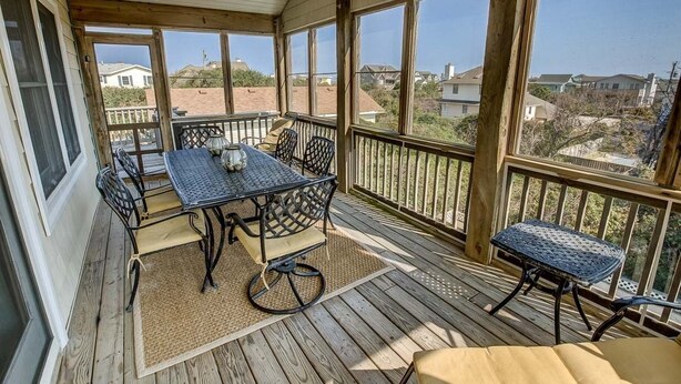 A covered outdoor patio with a table and chairs, large windows, and a view of the neighborhood. - Summer Place | 325 ft from the beach | Private Pool, Hot Tub | Southern Shores (Southern Shores)