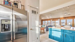 A modern kitchen with stainless steel appliances, a blue island, and a view of the living area. - Summer Place | 325 ft from the beach | Private Pool, Hot Tub | Southern Shores (Southern Shores)