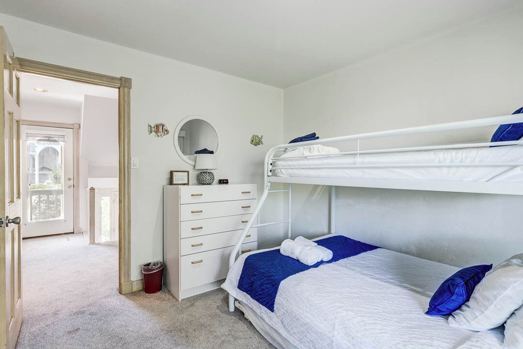 A bunk bed room with a white dresser, a mirror, and a door leading to a balcony.