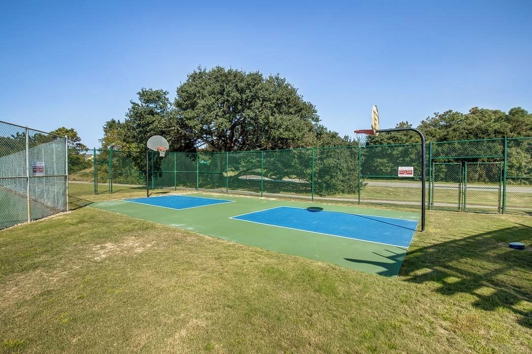 Een basketbalveld buiten, met twee blauwe velden, omgeven door een groene hekken en bomen op de achtergrond.