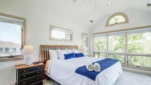 Une chambre avec un grand lit, deux tables de chevet et une vue sur la verdure grâce à de grandes fenêtres.