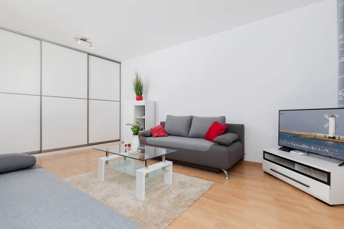 Ett modernt vardagsrum med en grå soffa, ett soffbord i glas och en platt-TV placerad på ett vitt TV-bord.