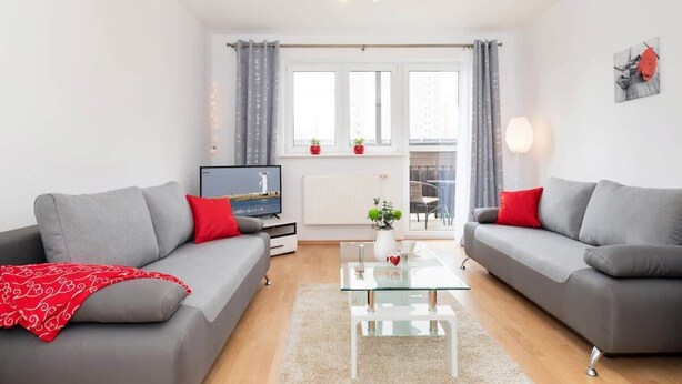 En moderne stue med to grå sofaer, et glasbord og et fjernsyn på et stativ.