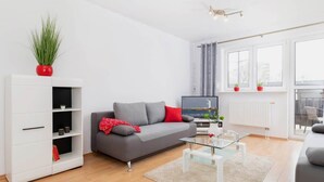 En moderne stue med en grå sofa, et hvidt skab, et glasbord og en rød plante.