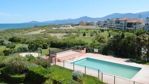 A pool area with a view of the sea and mountains, surrounded by greenery and a building with multiple balconies. - 2-room apartment with mezzanine, pool, and parking in Saint Cyprien (Saint-Cyprien)