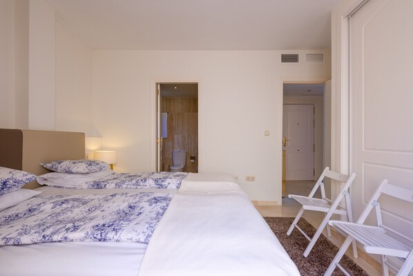 A hotel room with a bed, two white chairs, a nightstand with a lamp, and a door leading to another room. - Santa Maria, Marbella - Exclusive 2 level Penthouse, Sea View (Marbella)