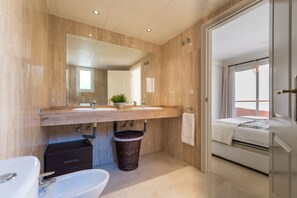 Ein modernes Badezimmer mit Waschtisch aus Holz, einem großen Spiegel, einem Waschbecken, einem Bidet und einer kleinen Topfpflanze.