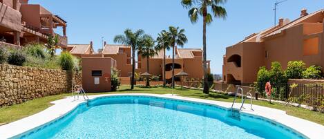 A swimming pool surrounded by buildings with a stone wall and palm trees.