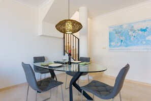 A dining area with a round glass table, four grey chairs, a hanging light fixture, and a world map on the wall. - Santa Maria, Marbella | Charming 2-Level Penthouse with Terraces, BBQ & Mediterranean Views in Marbella (Marbella)