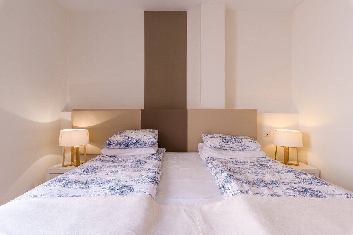 A double room with two beds, each with a nightstand and a lamp.