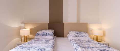 A double room with two beds, each with a nightstand and a lamp.