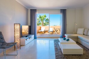 A modern living room with a flat-screen TV, a sofa, a coffee table, and a view of a balcony with outdoor furniture. - Santa Maria, Marbella - Exclusive 2 level Penthouse, Sea View (Marbella)