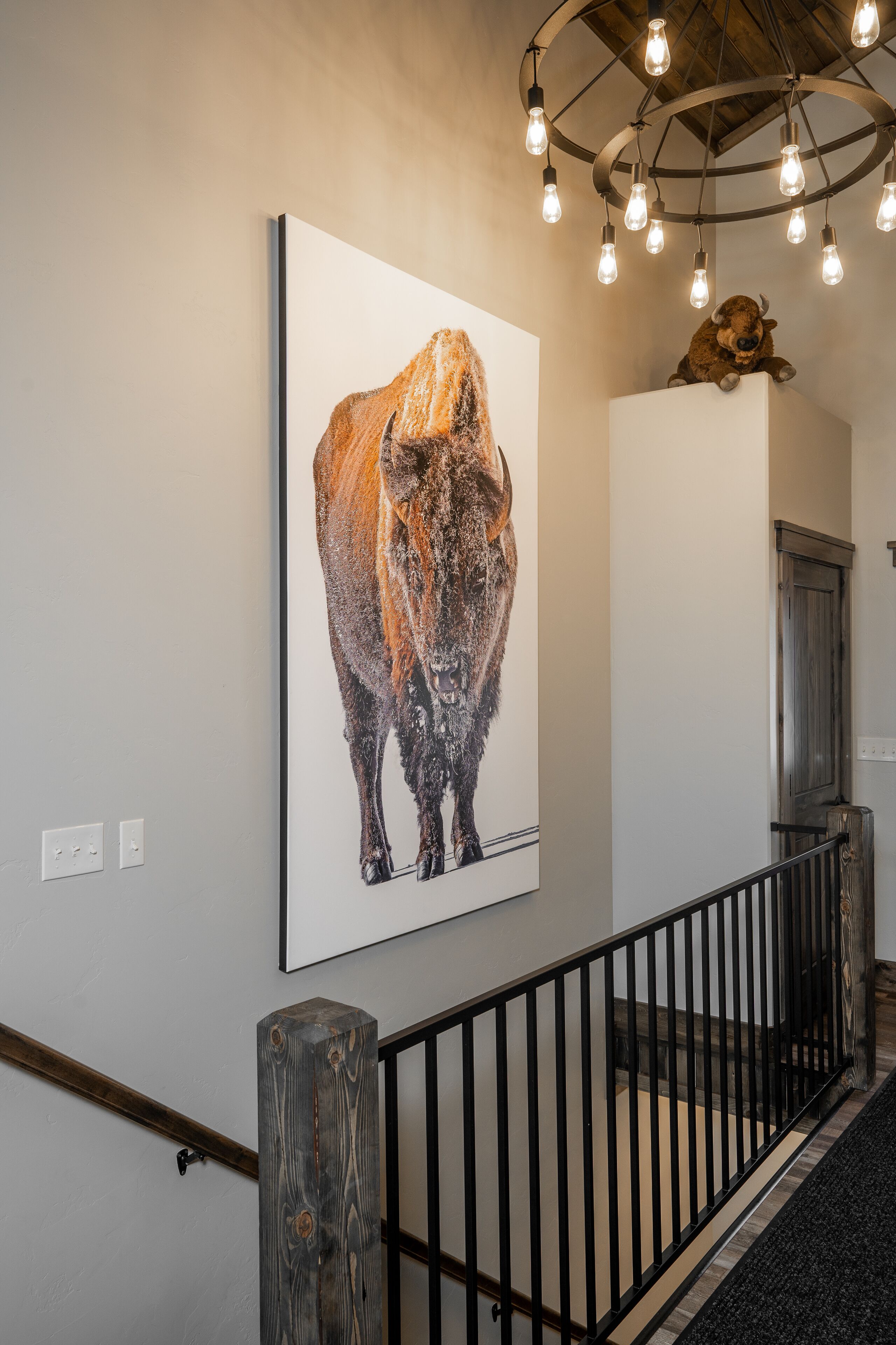 A hallway with a large framed artwork of a bison, a wooden railing, and a ceiling with exposed beams and hanging lights.