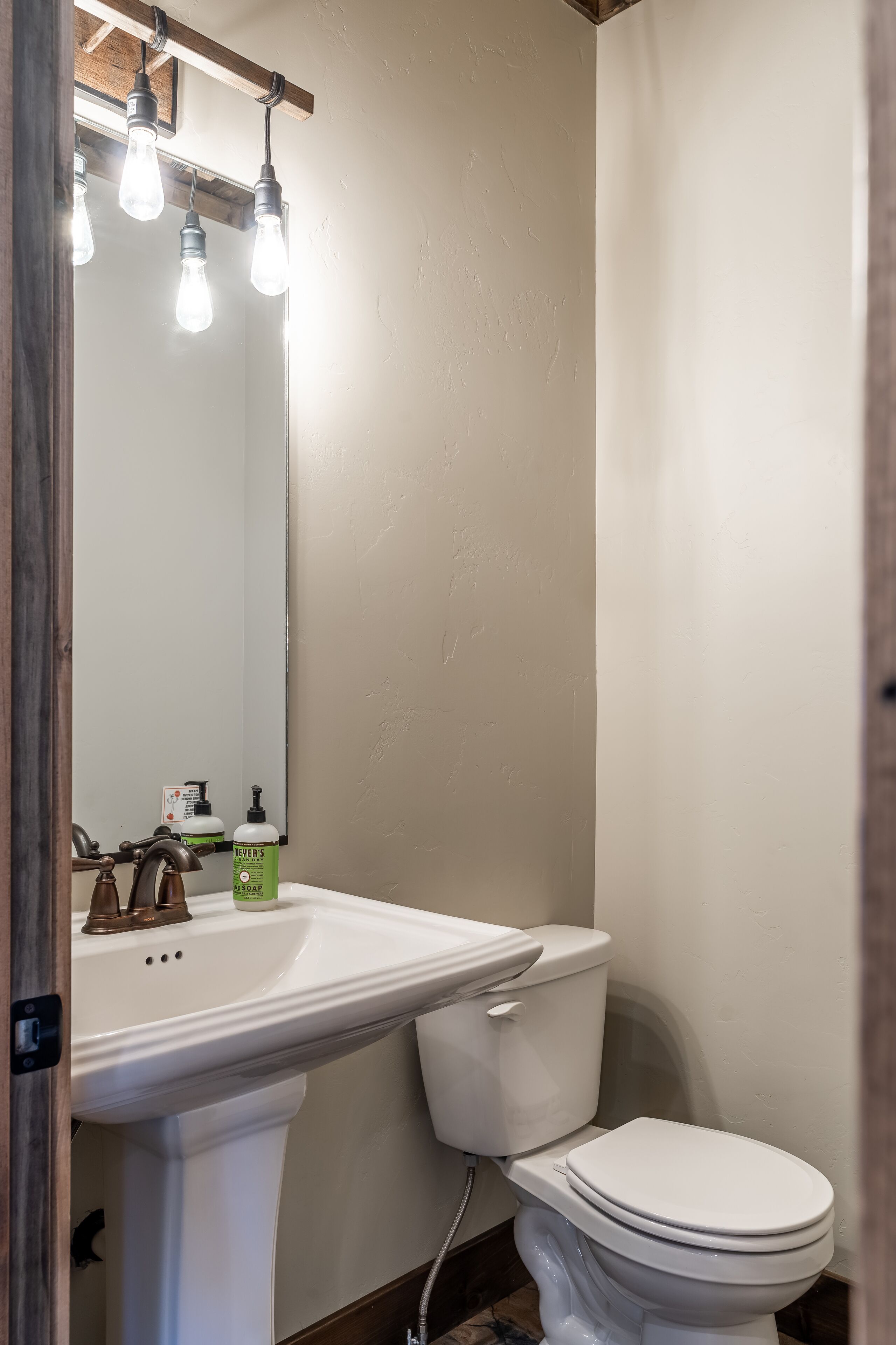 A bathroom with a white sink, a toilet, and a mirror. There are three light bulbs above the mirror.