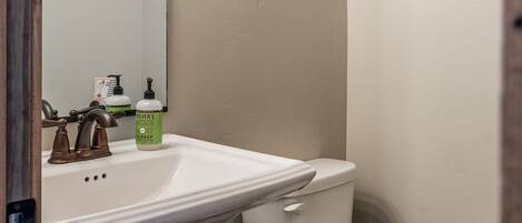 A bathroom with a white sink, a toilet, and a mirror. There are three light bulbs above the mirror.