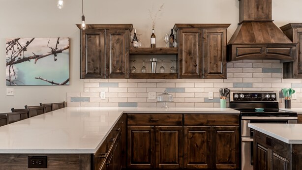 Une cuisine moderne avec des meubles en bois foncé, un grand îlot central et une cuisinière intégrée.