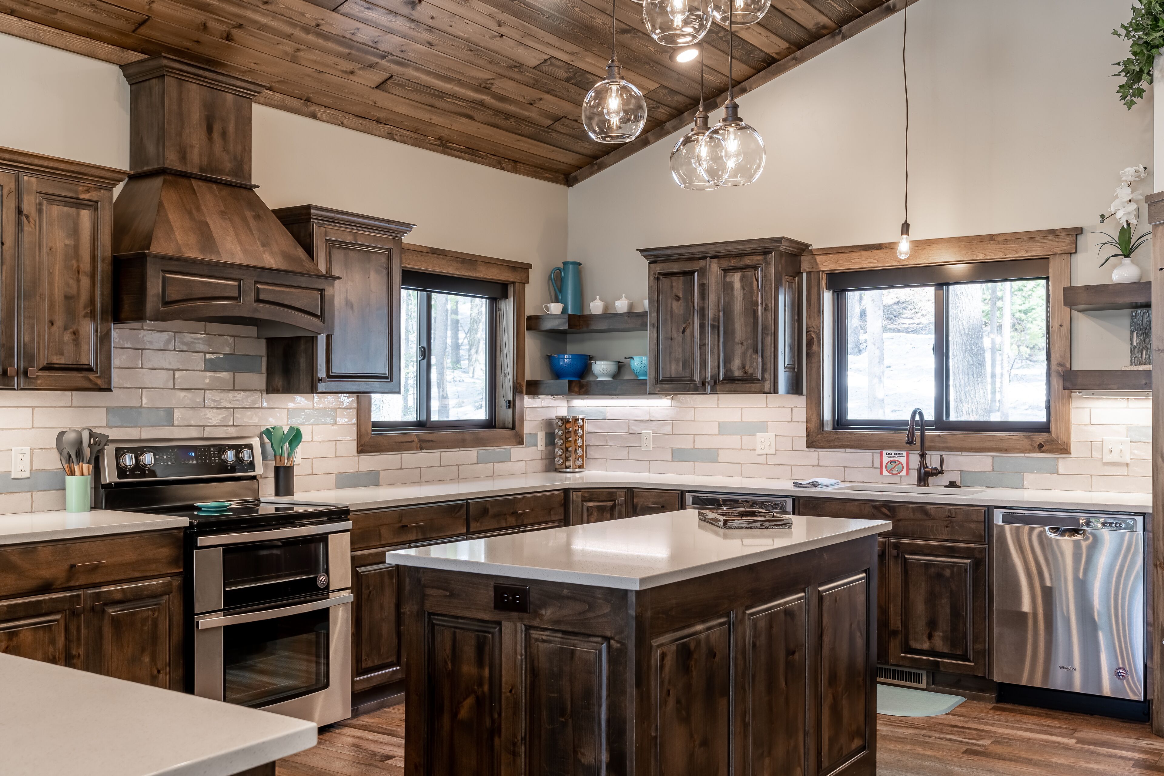 Una cocina moderna con armarios de madera oscura, una isla central, electrodomésticos de acero inoxidable y techo de estilo campestre.
