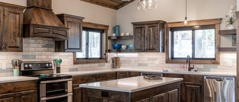 Una cocina moderna con armarios de madera oscura, una isla central, electrodomésticos de acero inoxidable y techo de estilo campestre.