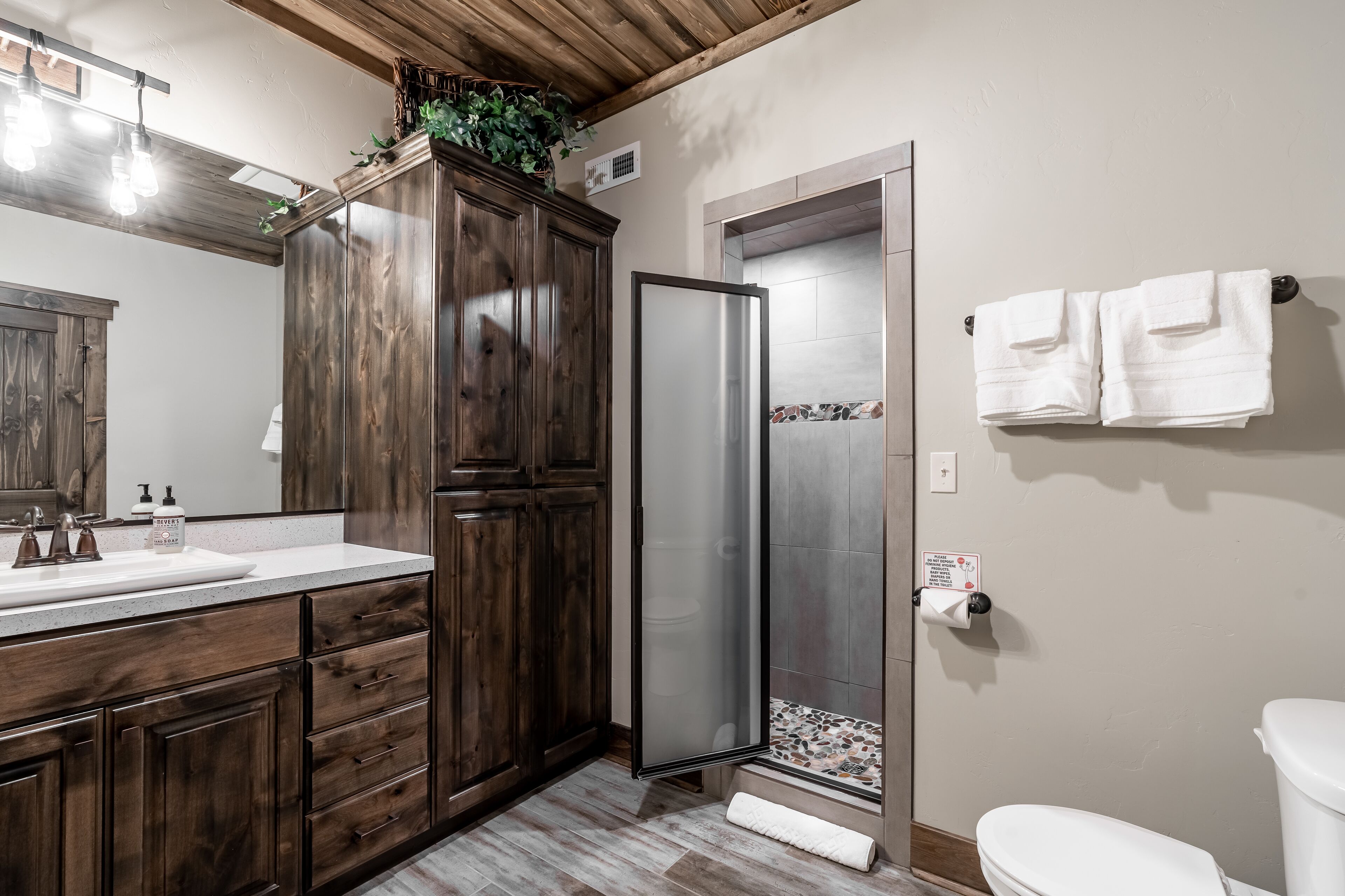 Une salle de bain avec un meuble-lavabo en bois, une douche dotée d’une porte en verre dépoli et un porte-serviettes.