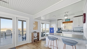 Een moderne keuken met een groot kookeiland, barkrukken en uitzicht op het strand door de schuifdeuren.
