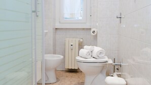 A bathroom with two toilets, a towel rack, and a window.