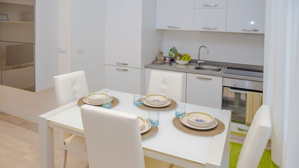 A modern kitchen with white cabinetry, a dining table set with plates and glasses, and a built-in oven.