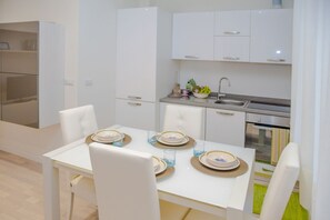 Une cuisine moderne avec des meubles blancs, une table à manger dressée avec des assiettes et des verres, et un four encastré.