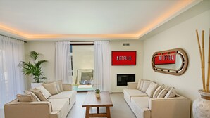 A modern living room with two beige sofas, a wooden coffee table, and a TV mounted on the wall. - 100m from the beach, hot tub, ping pong, sauna, gym & private sun beds! (Rethymno)