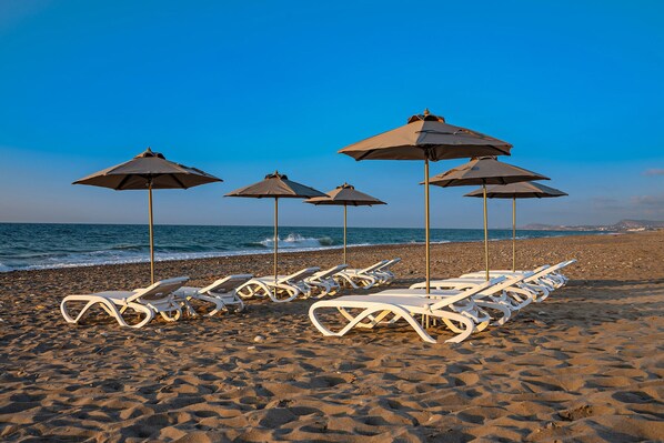 A beach with white lounge chairs and umbrellas arranged in rows.