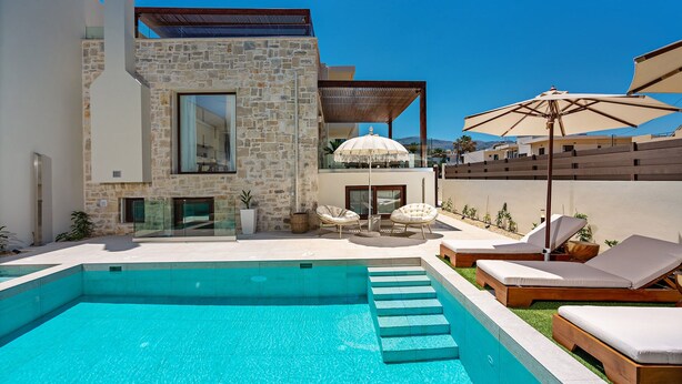 A modern pool area with a stone building, lounge chairs, and umbrellas. - 100m from the beach, hot tub, ping pong, sauna, gym & private sun beds! (Rethymno)