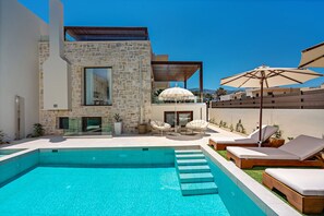 A modern pool area with a stone building, lounge chairs, and umbrellas.