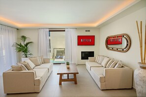 Un salon moderne avec deux canapés beige, une table basse en bois et un téléviseur fixé au mur.