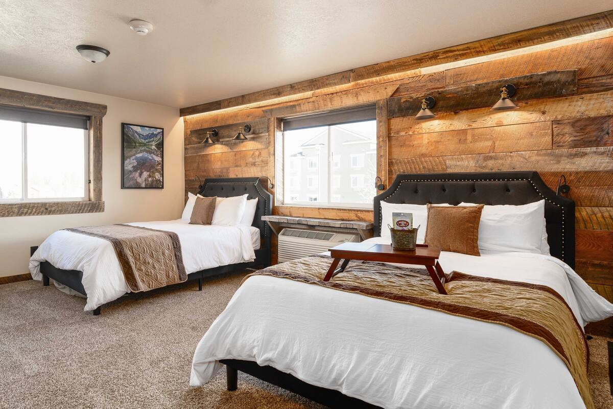 A hotel room with two beds, a wooden accent wall, and a large window.