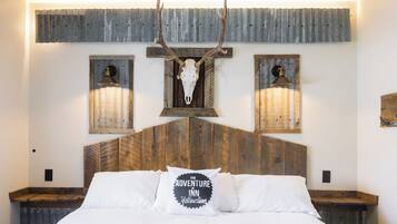 A bed with a wooden headboard, a wall-mounted deer skull, and two wall sconces.