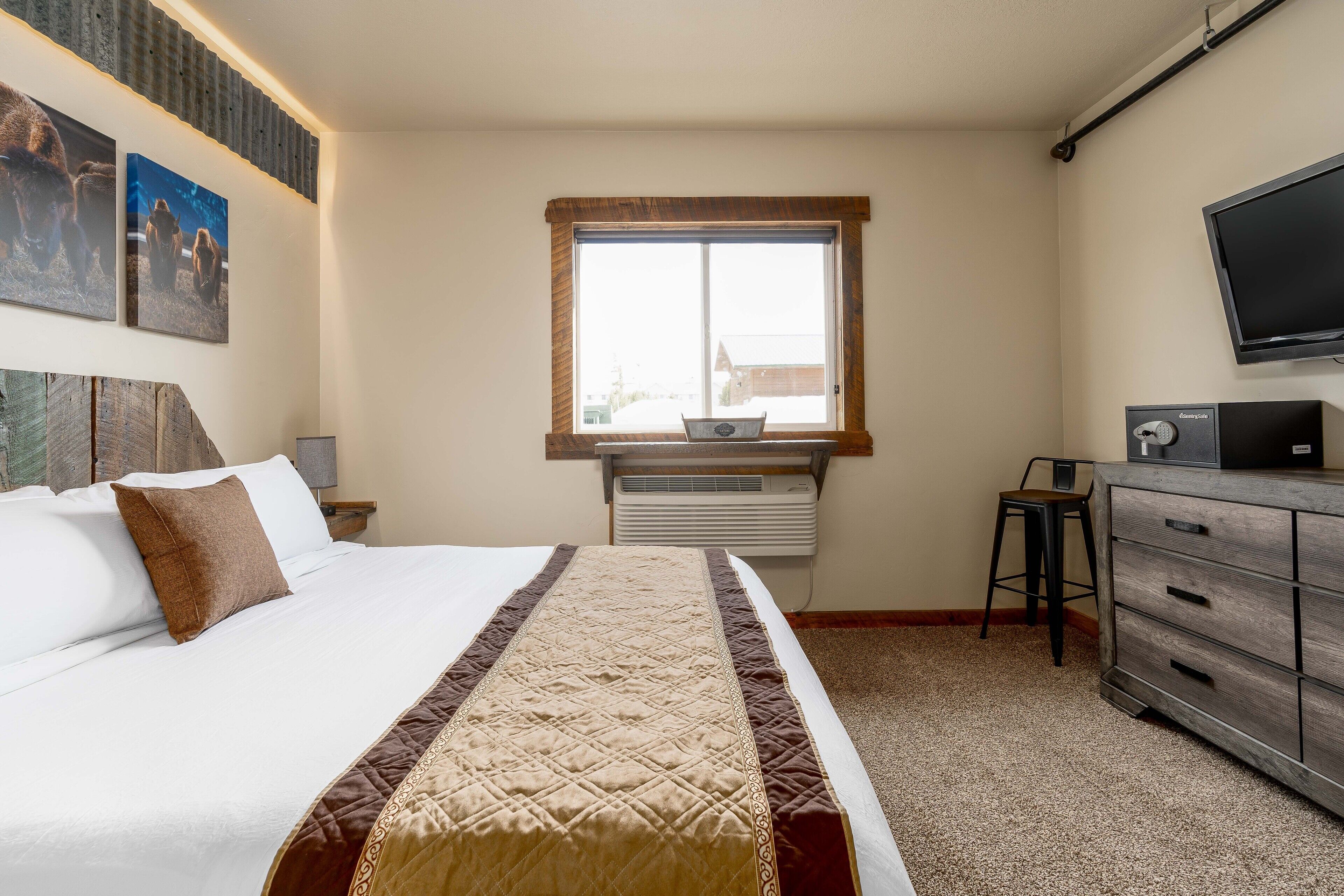 Habitación de hotel con cama, escritorio con computadora, televisor y ventana con vista a edificios.