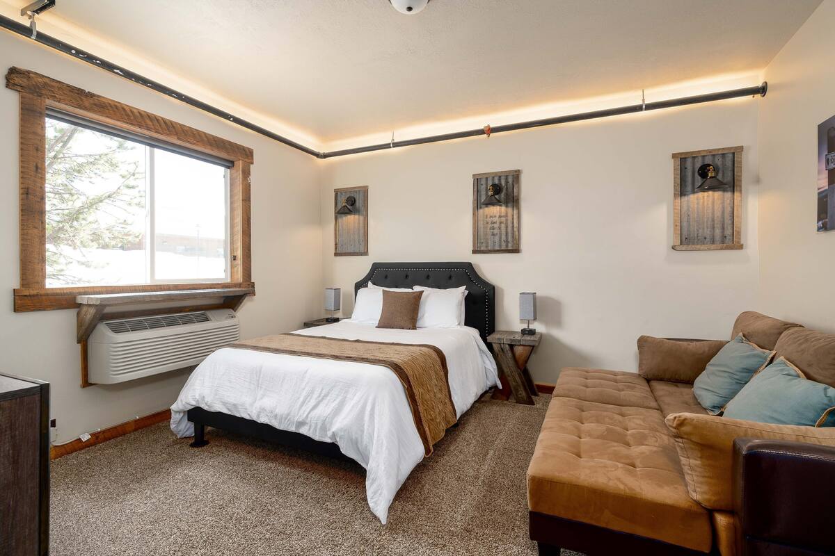 A bedroom with a bed, a sofa, a window, and wall-mounted lamps.