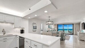 A modern kitchen with white cabinetry, a central island, and a dining area with a view of the ocean. - Gulf View Balcony ~ Seasonally Heated Pool (Miramar Beach)