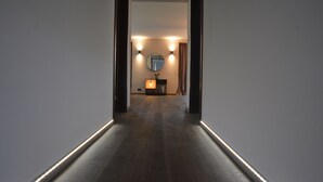 Un pasillo con piso de madera que conduce a una habitación con un espejo redondo, una mesita y dos luces empotradas en la pared.