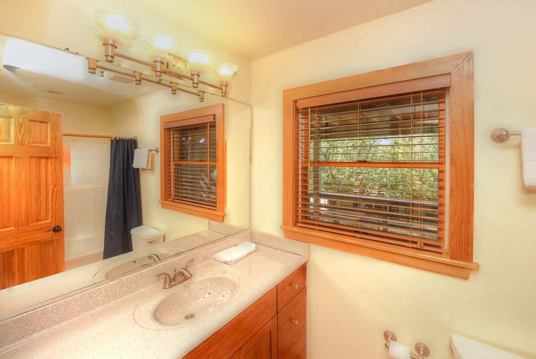 A bathroom with a sink, mirror, wooden cabinets, and a window with blinds.