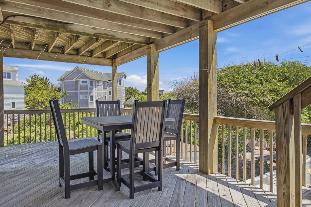 A covered outdoor deck with a table and chairs, wooden railings, and a view of residential buildings.