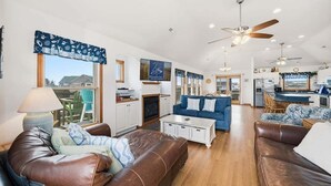 A spacious living room with leather sofas, a coffee table, and a fireplace. There is a kitchen in the background with a dining area. - Five Lucky Ducks | 400 ft from the beach | Dog Friendly, Private Pool, Hot Tub | Duck (Duck)