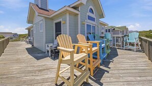 A wooden deck with Adirondack chairs, a small building with a pitched roof, and a clear blue sky. - Five Lucky Ducks | 400 ft from the beach | Dog Friendly, Private Pool, Hot Tub | Duck (Duck)