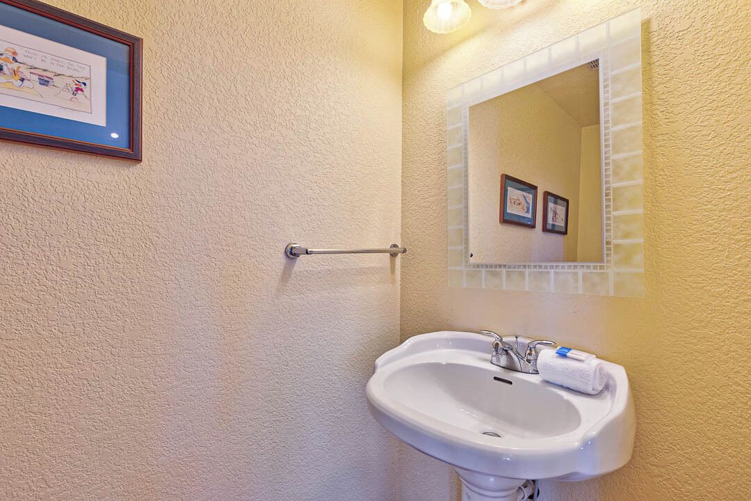 Une salle de bain avec un lavabo blanc, une serviette, un tableau encadré et un miroir avec un cadre blanc.