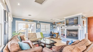 A living room with a fireplace, a sofa, a coffee table, and a bookshelf. - No Wake Zone | 164 ft from the beach | Dog Friendly, Hot Tub | Nags Head (Nags Head)