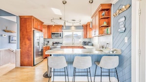 A modern kitchen with wooden cabinets, a central island with bar stools, and pendant lighting. - No Wake Zone | 164 ft from the beach | Dog Friendly, Hot Tub | Nags Head (Nags Head)