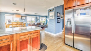 A modern kitchen with wooden cabinets, a stainless steel refrigerator, and a large island with a granite countertop. - No Wake Zone | 164 ft from the beach | Dog Friendly, Hot Tub | Nags Head (Nags Head)