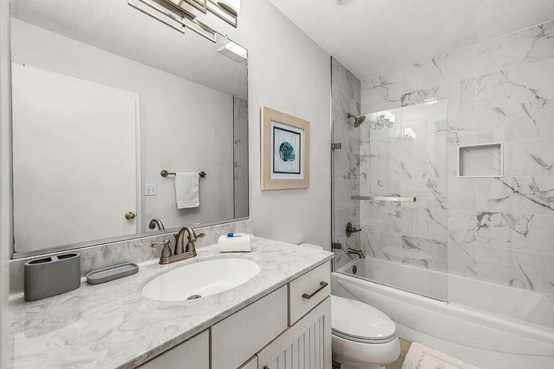 Un baño con un espejo grande, dos lavamanos, un inodoro y una ducha con paredes de mármol.